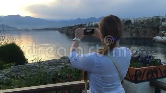 年轻女子在日落时拍了一张风景照带着智能手机的白人女孩拍了一张风景照片视频的预览图