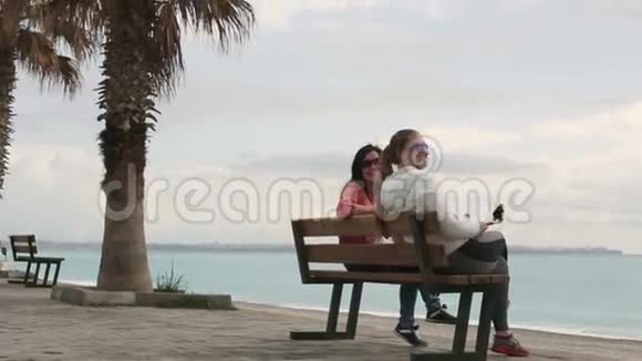 两个年轻的女人坐在海边用智能手机手机相机拍摄自己的肖像特写镜头高清高清视频的预览图