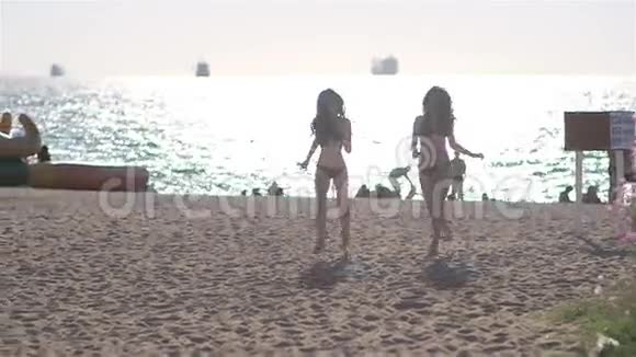 两个穿比基尼的年轻漂亮女孩在海滩上散步视频的预览图