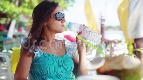 开朗的女孩戴着太阳镜在海滩咖啡馆喝水1920x1080视频的预览图