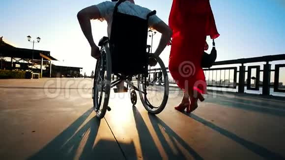 在夏日的夜晚带着病腿的男人在轮椅上与女友在水边散步视频的预览图