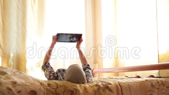 年轻的阿拉伯女孩带着平板电脑在家里卧室的床上女人反映在屏幕上技术与人的概念视频的预览图
