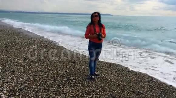 美丽的女人拿着相机站在海滩上视频的预览图