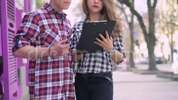 成功的女孩和男孩微笑着在街上用笔记本和电话视频的预览图