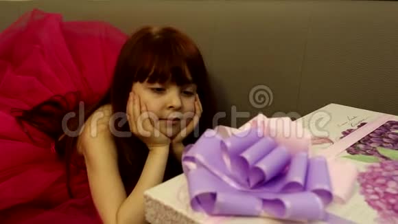 可爱快乐兴奋的女孩穿着令人惊叹的粉红色连衣裙等待着看紫色丝带的巨大礼品盒视频的预览图