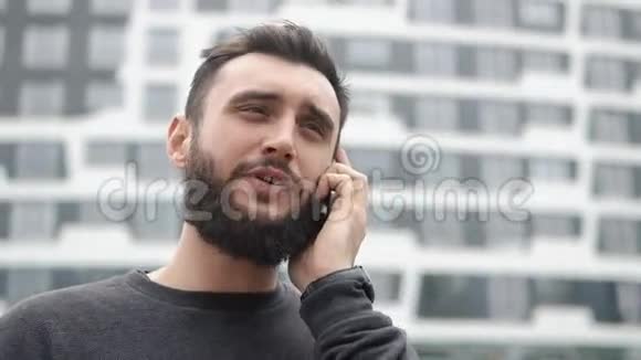 有胡子的年轻人在高楼附近打电话视频的预览图