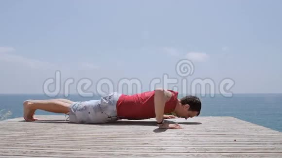 白人运动员在阳光明媚的日子在岩石海岸海滩上做俯卧撑视频的预览图