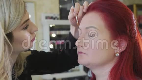 化妆师给美容店的年轻红发女人做漂亮的眉毛视频的预览图