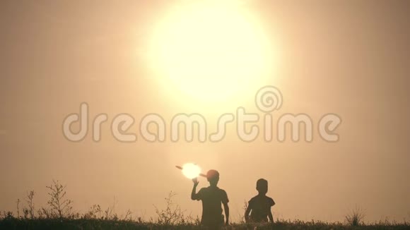 两个男孩在日落时玩一架木飞机儿童玩飞机的剪影飞行的梦想概念视频的预览图