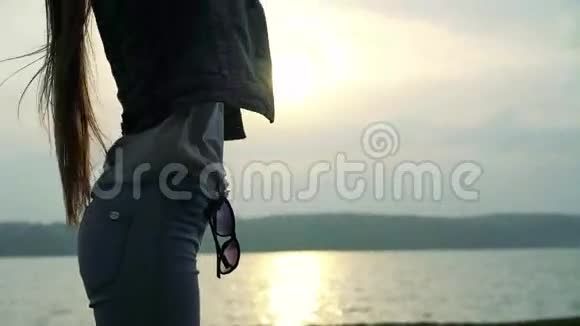 女孩站着在海上背景的夕阳上抚摸着她的头发4k视频的预览图