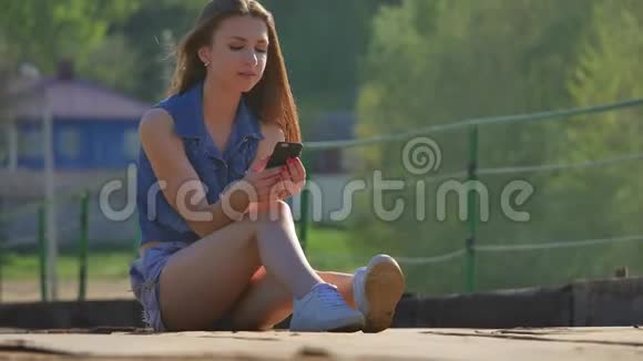 那个女孩拿着一部智能手机网络女孩户外智能手机社交媒体坐在铁桥上视频的预览图