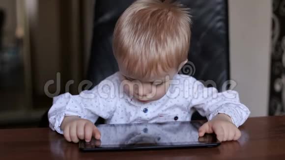 小男孩拿着平板电脑坐在桌子旁视频的预览图