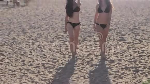 日落时分两个穿着比基尼的年轻漂亮女孩在海滩上散步视频的预览图
