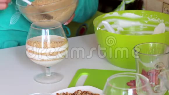 一个女人在制作甜点时加入一层玻璃材料饼干面包屑和奶油附近有一个草莓视频的预览图