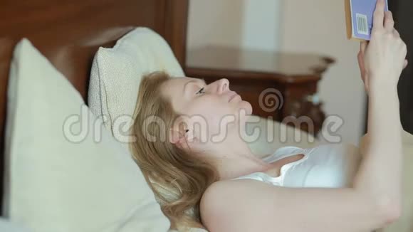 美丽的年轻女子在床上看书视频的预览图