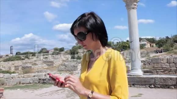 有魅力的女人在古城遗址和海洋背景上使用智能手机视频的预览图