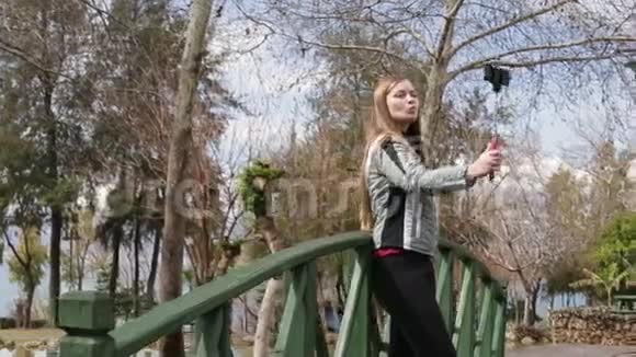 年轻快乐的女人用智能手机手机相机在木桥上拍摄自己的肖像特写视频的预览图