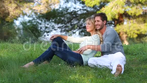 美丽的夫妇坐在绿色的草地上视频的预览图