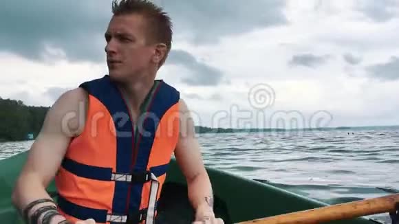 一个坐在船上划木桨的年轻人人身上的救生衣视频的预览图