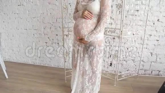 美丽的孕妇穿着连衣裙站在窗口视频的预览图