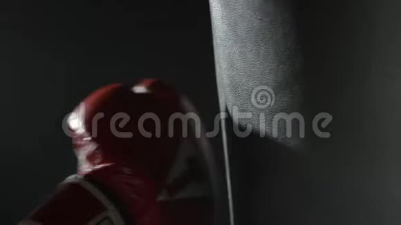 年轻的男拳击手在黑色背景上打拳在健身房里用红色拳击手套打孔袋MMA视频的预览图