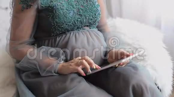 怀孕母性微笑的孕妇坐在沙发上用平板电脑视频的预览图