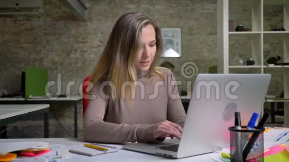 一位美丽的成年女士在办公室的笔记本电脑上打字微笑着视频的预览图