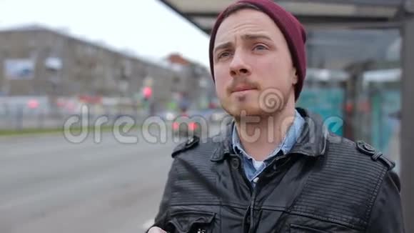 有魅力的男人在城市汽车站等着看手机视频的预览图