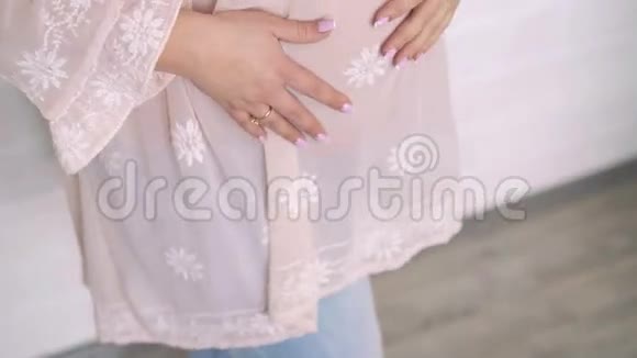 温柔的孕妇在米色背景上抚摸她的腹部4k视频的预览图