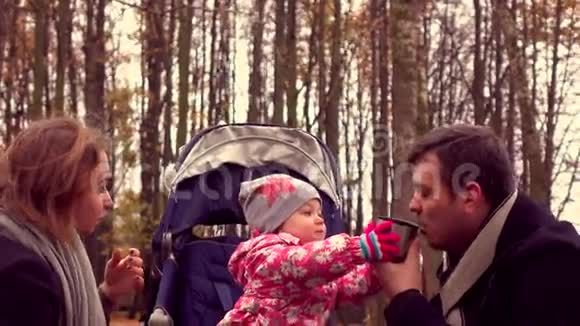 可爱的小女孩和她的父母在秋天公园喝着热气腾腾的茶家庭野餐4Ksteatam视频视频的预览图