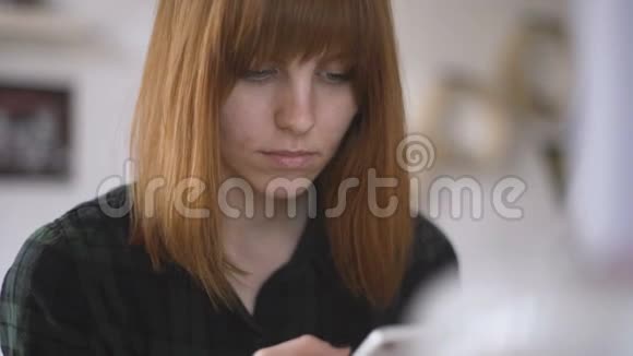 年轻漂亮的红发女郎在家里使用智能手机视频的预览图