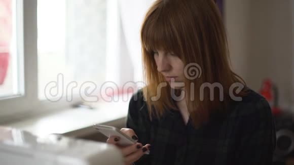 年轻漂亮的红发女郎在家里使用智能手机视频的预览图