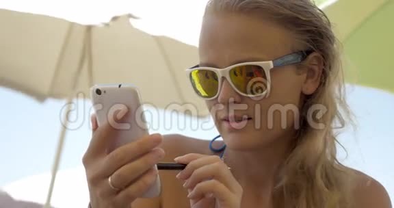 戴太阳镜的女人在海滩上用手机视频的预览图