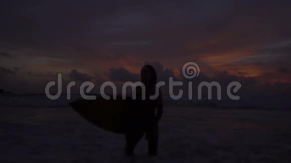美丽的女人带着冲浪板在令人惊叹的日落中的剪影视频的预览图