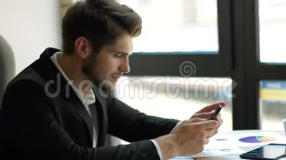 预期的信息年轻的帅哥在工作场所微笑着使用智能手机视频的预览图