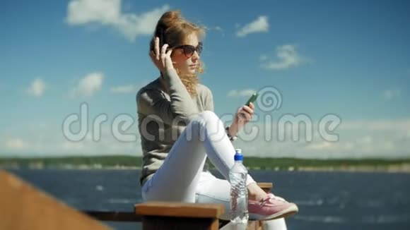 女人喜欢在海滩上用耳机听音乐的智能手机视频的预览图