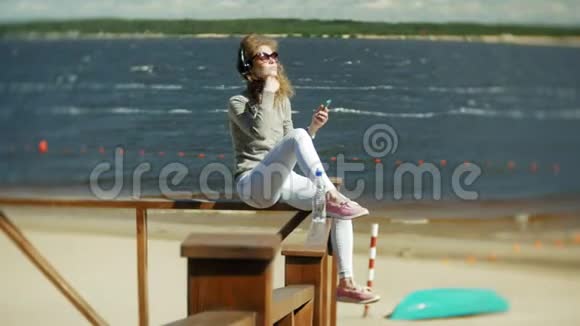 女人喜欢在海滩上用耳机听音乐的智能手机视频的预览图