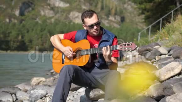 阳光明媚的一天戴着太阳镜的人在河边坐着吉他4k3840x2160视频的预览图
