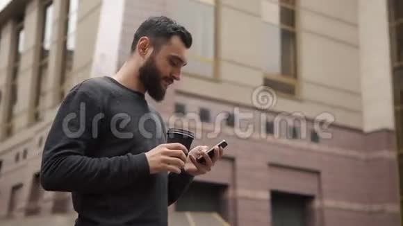 快乐的胡子年轻人在智能手机上发短信日落时分在街上喝咖啡视频的预览图