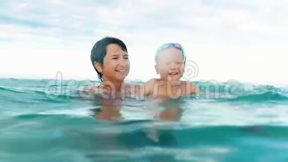快乐的儿子和母亲微笑着看着镜头在海上缓慢的动作中飞溅视频的预览图