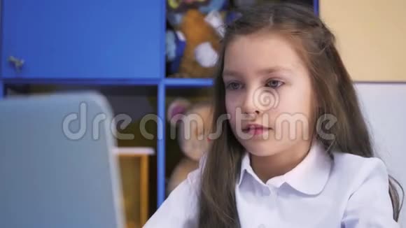 在图书馆学习的女孩用笔记本电脑做课后作业有设备的小学儿童视频的预览图