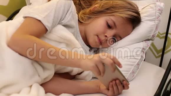 小女孩在床上用智能手机发短信视频的预览图