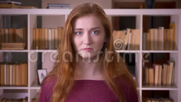 在大学图书馆里一位年轻的红头发迷人的白种人女学生看着摄像机的特写镜头视频的预览图
