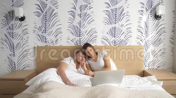 一对笑着的夫妇用笔记本电脑躺在床上视频的预览图