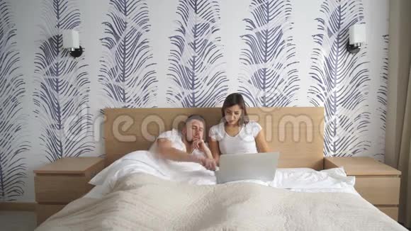 一对快乐的夫妇在家里躺在床上用电脑视频的预览图