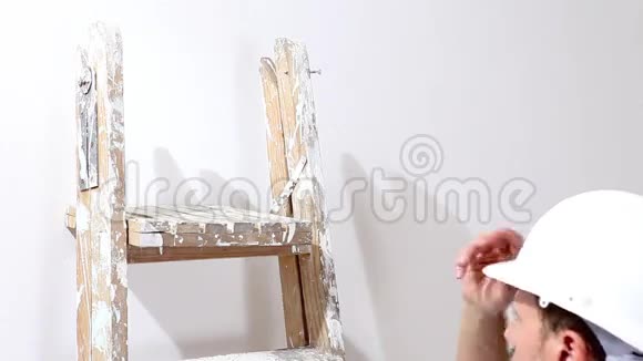 油漆工在工作时将头盔支撑在梯子上油漆到墙上视频的预览图