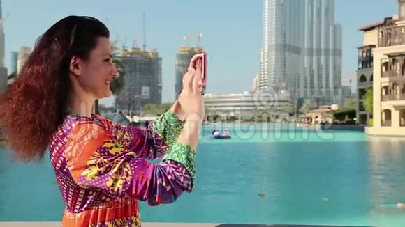 漂亮的女人站在蓝色游泳池附近在他的智能手机上拍照视频的预览图