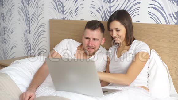 年轻夫妇带着笔记本电脑在床上看电影视频的预览图