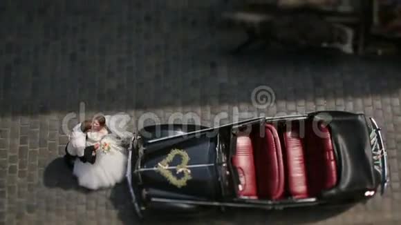 当马车经过时一对迷人的新婚夫妇在城市道路上的复古汽车前亲吻俯视图视频的预览图