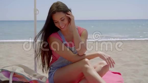 女人坐在沙滩的阴凉处手挽着脖子视频的预览图
